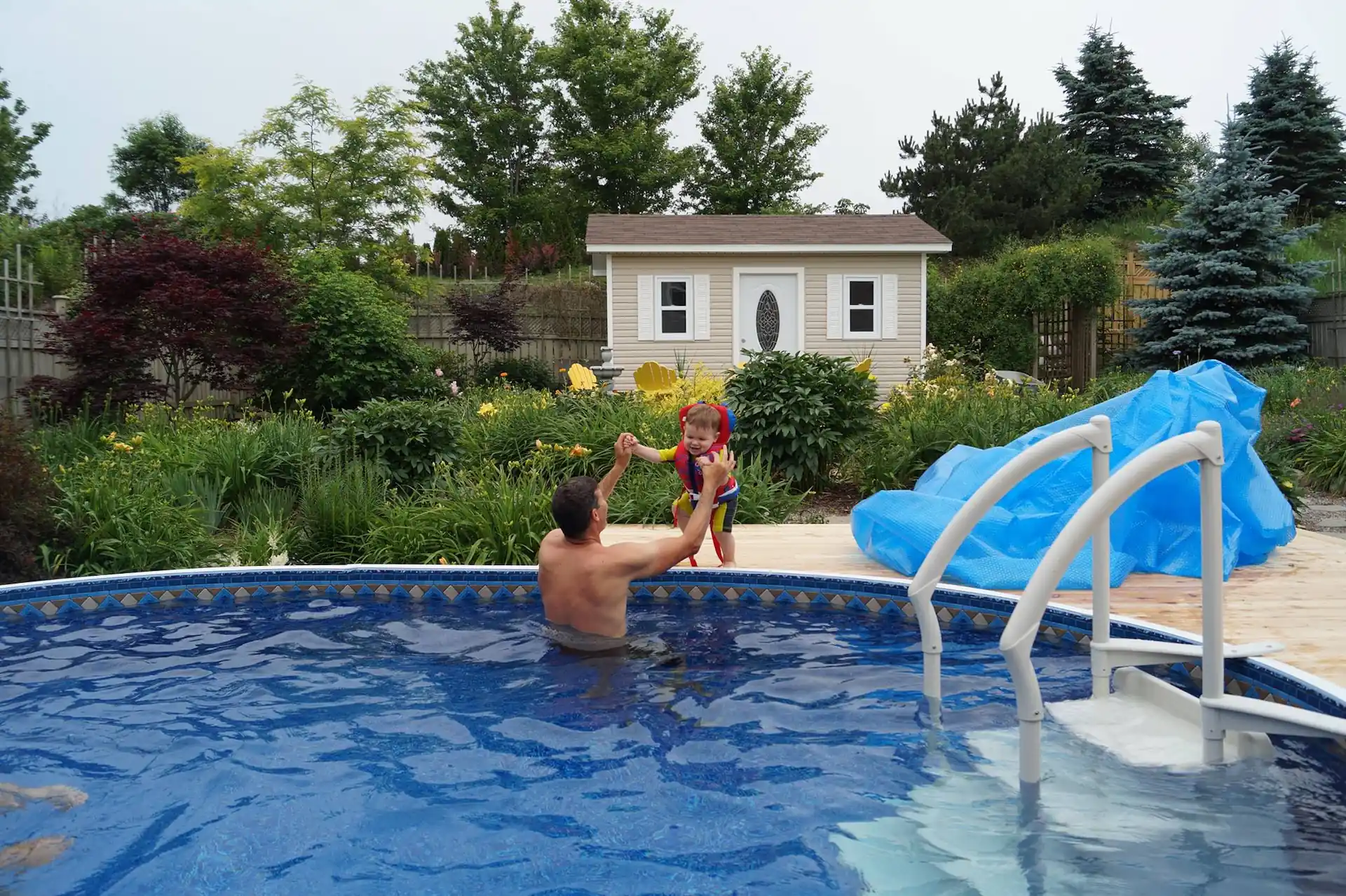 An adult swimmer helps a small child wearing floatation gear into an above ground pool.