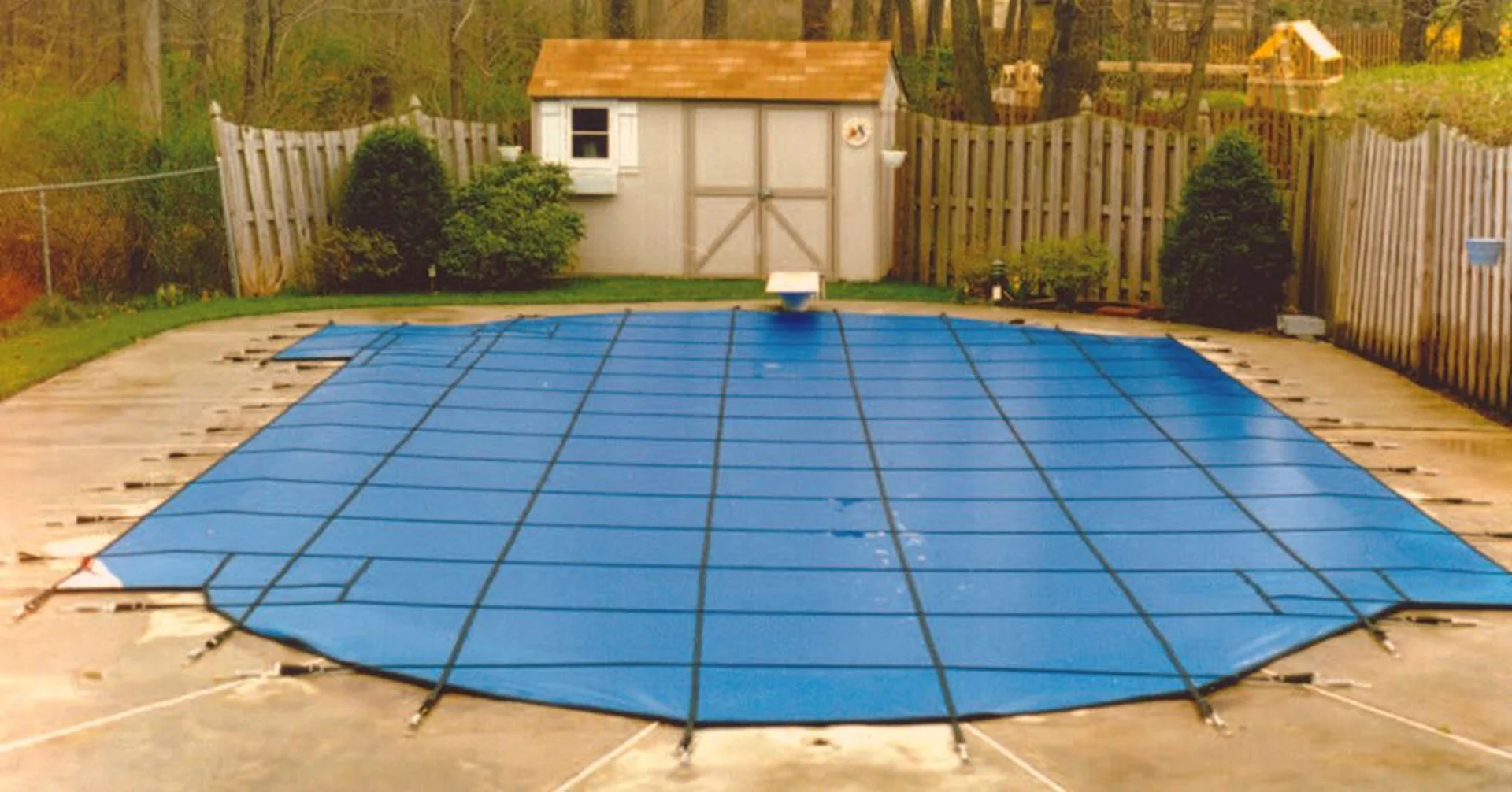 A blue safety cover is fastened to an inground pool in Pennsylvania. A safety cover is a good pool cover solution for winter.