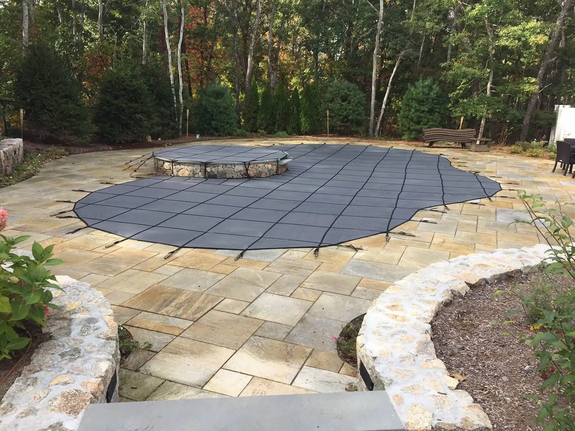 A dark-colored pool safety cover is stretched across a curved inground pool and spa in the Pennsylvania outdoors.