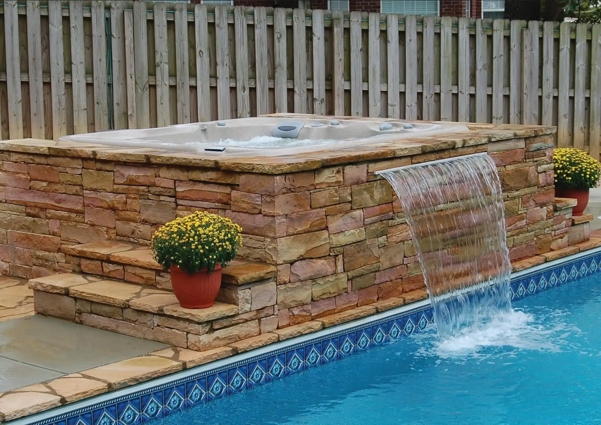A pool and hot tub combo complete with a concrete surround and a water cascade.