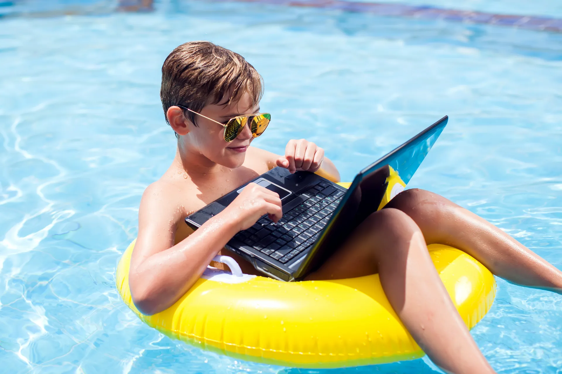 A swimmer wearing sunglasses types on a laptop resting on their lap while sitting in a round
