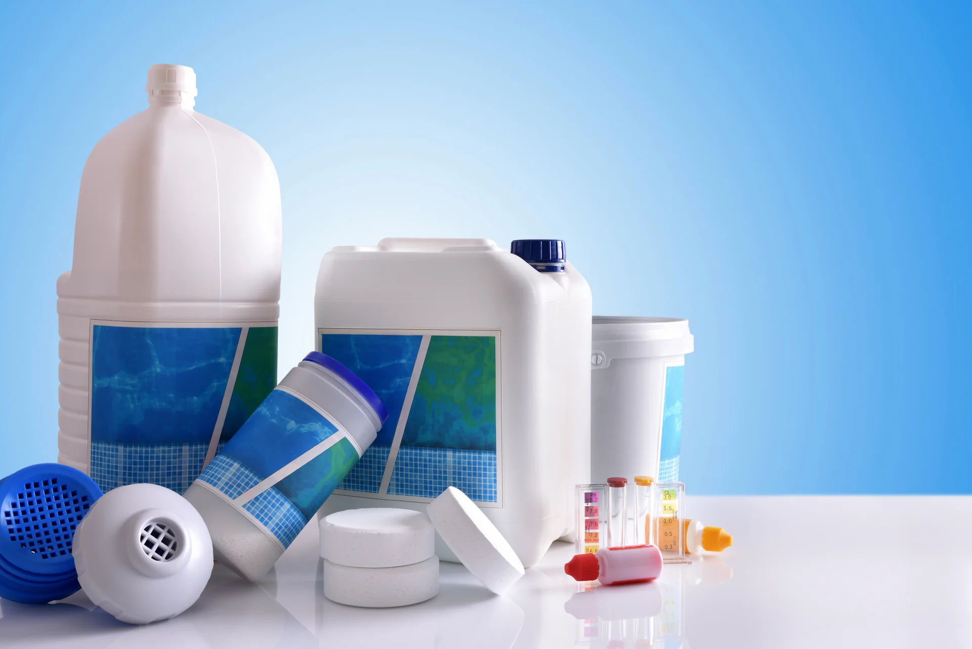 Various pool chemicals contained in bottles and tablets sit on a tabletop. Multiple chemicals are included in a pool closing kit.
