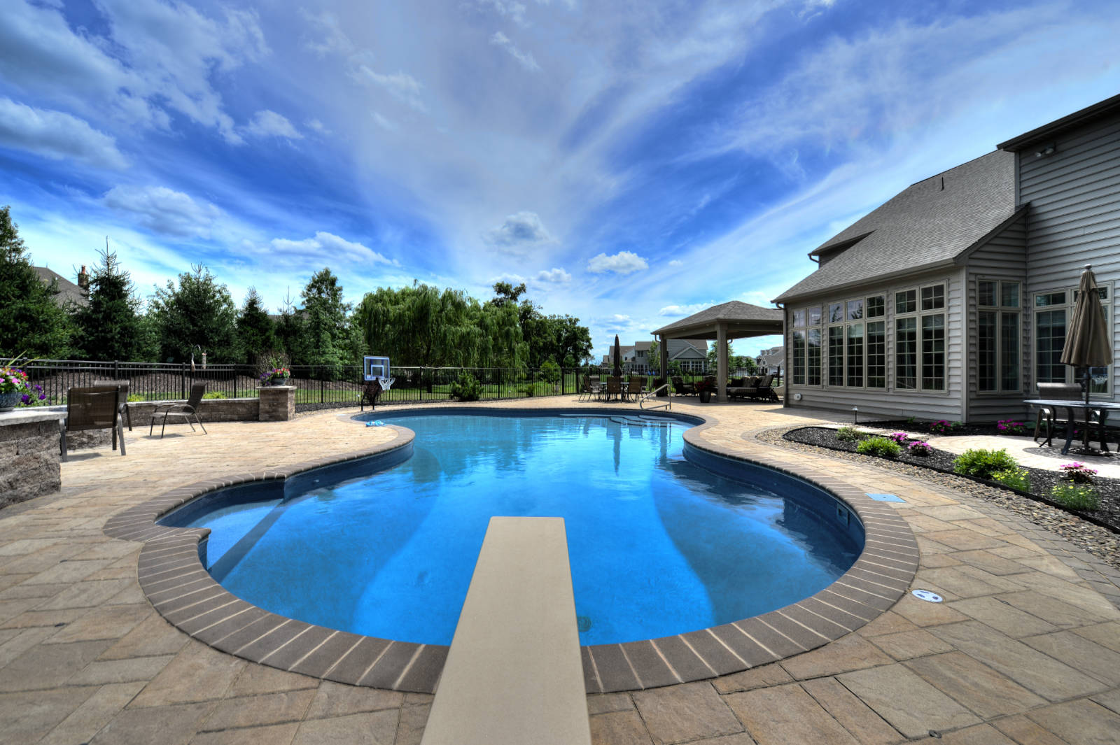 An inground pool with a diving board in a backyard.